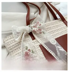 Close-up of straw woven tote bag featuring floral lace bow and brown leather strap detail