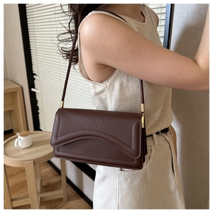 Detail of a dark brown leather underarm bag with gold metal buckle and model lifestyle shot