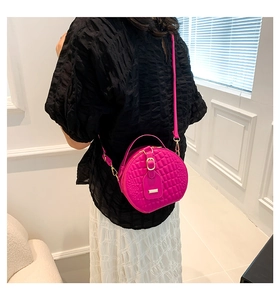 Model wearing a round magenta crossbody bag with crocodile texture and gold buckle detail