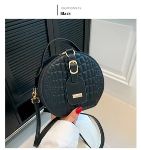 Detail of a black round crossbody bag featuring quilted crocodile texture and top handle