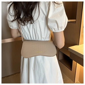 Sac baguette beige à texture crocodile avec logo doré porté par un modèle en robe