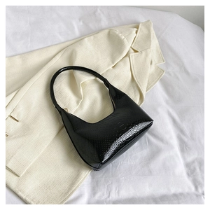 Dettaglio borsa hobo nera con trama a coccodrillo su blazer beige e tessuto bianco