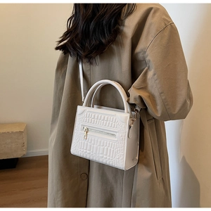 White crocodile pattern handbag styled with a brown trench coat for a classic casual look