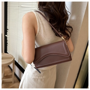 Detail of dark brown leather shoulder bag with gold hardware worn as an underarm bag