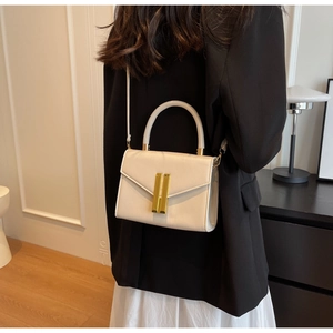 Detail shot of the cream crossbody bag with golden vertical bars and hard handle grip