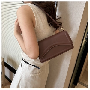 Detail view of a brown leather shoulder bag with unique layered flap and gold hardware