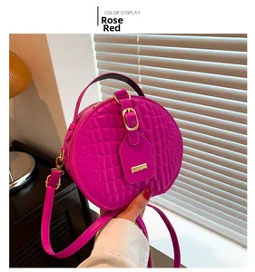 Detail of rose red round bag with crocodile texture and gold hardware held by hand