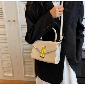 Detail of white leather crossbody bag with iconic gold bar lock on a black suit background