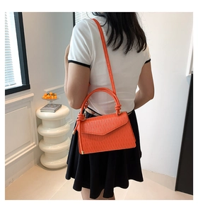 Detail view of the orange crossbody bag showing textured PU leather and stylish handle