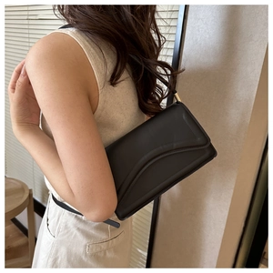 Close-up of minimalist black leather underarm bag worn on shoulder in home setting