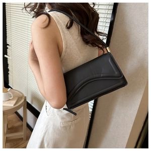 Chic black shoulder bag with curved flap and gold hardware worn by model in home setting