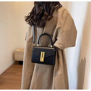 Detail of elegant black leather crossbody bag with vertical gold lock on a minimalist model