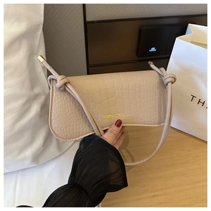 Détail du sac à main beige à motif crocodile avec bandoulière à nœuds dorés