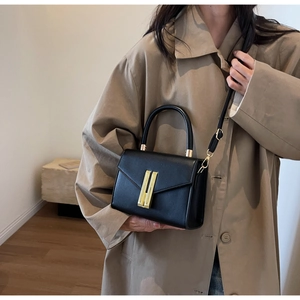 Detail of a black leather crossbody bag featuring a vertical gold metal buckle and strap