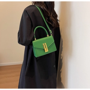Close-up of vibrant green leather crossbody bag with gold buckle on model with trench coat