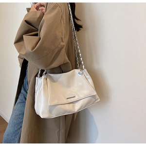 Détail du sac à bandoulière blanc crème avec chaîne sur un trench-coat kaki chic