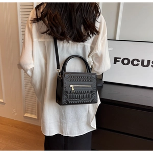Detail of black crossbody bag with geometric embossed texture and gold zipper accent
