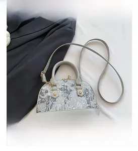 Detail view of grey shell bag with floral pattern, gold zippers, and leather straps
