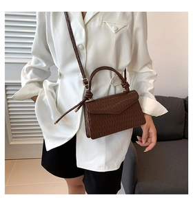 Detail of a brown pleated crossbody bag with a knotted handle and structured square shape