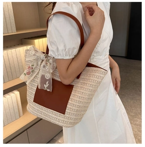 Détail d'un sac cabas en paille tissée avec garniture en cuir brun et nœud floral en dentelle