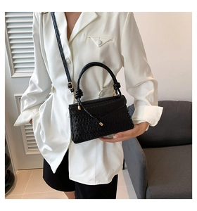 Detail of black embossed leather handbag with metal buckle worn by model in white suit