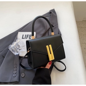 Close-up of black crossbody bag on grey blazer with large gold rectangular metal buckle