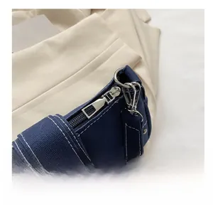 Detail view of smooth silver metal zipper and white stitching on navy canvas shoulder bag