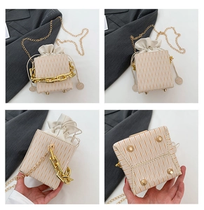 Detail of off-white textured bucket bag showing golden chain and drawstring closure