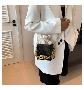Detail of black textured bucket bag with chunky gold chain on white blazer model