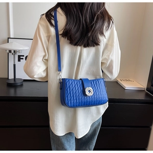 Rear view of a blue quilted crossbody bag with a silver twist-lock on a female model