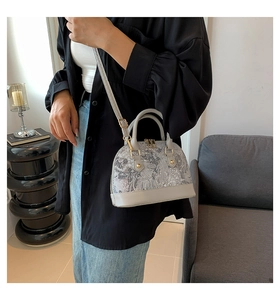Close-up of light gray shell bag with paisley print and dual zippers held by a model