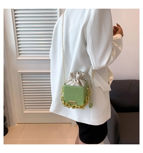 Green pleated bucket bag with gold chain strap shown on model in white blazer