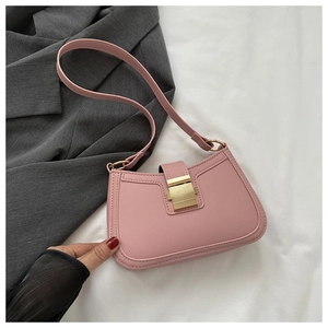 Sac sous le bras en similicuir rose avec boucle dorée posé sur une veste de blazer grise