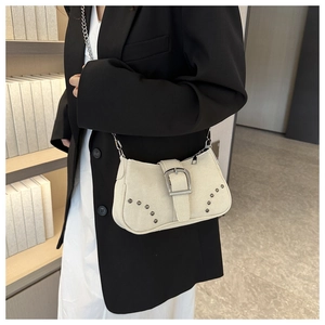 Detail view of beige canvas shoulder bag featuring metal rivets and silver buckle closure