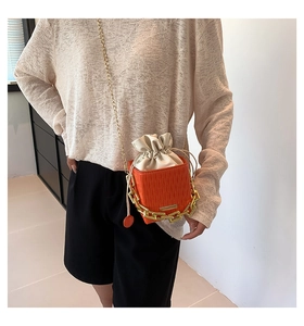 Detailed view of orange textured leather bucket bag with white drawstring and gold chain