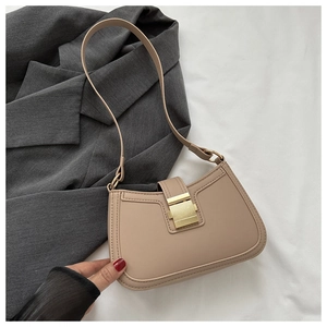 Détail d'un sac sous le bras en cuir beige avec boucle dorée sur un costume sombre