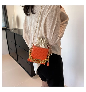 Detail of orange pleated bucket bag with bold gold chain and drawstring closure