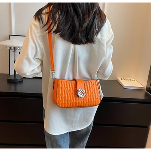 Close-up of orange crossbody bag with geometric quilting and silver metal knot buckle