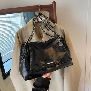 Sac fourre-tout en cuir noir brillant avec chaîne argentée sur un manteau neutre