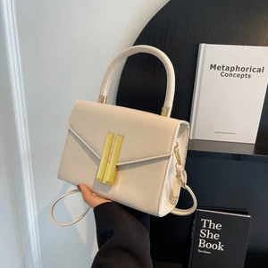 Minimalist beige leather crossbody bag with gold hardware and top handle shown in lifestyle