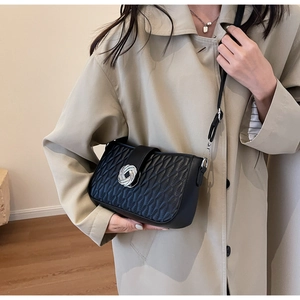 Detail of black wave-quilted shoulder bag featuring a silver knot metal buckle on coat