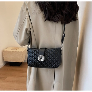 Detail of a black quilted crossbody bag with a round silver lock on a beige trench coat