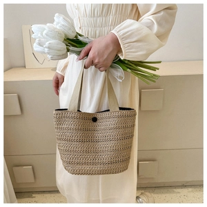 Detail of a beige woven tote bag with a black button closure and fabric handle