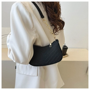 Detail of black quilted shoulder bag featuring gold chain strap on a minimalist model