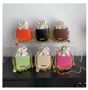 Close-up of six colorful pleated drawstring mini bags with gold chain straps on a shelf