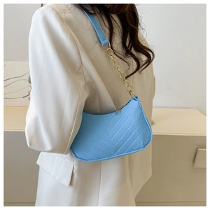 Detail of light blue quilted shoulder bag with gold chain strap on beige blazer