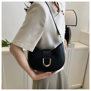 Sac à bandoulière noir en forme de croissant avec fermoir doré porté par une femme