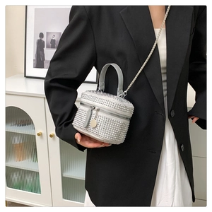 Detail shot of a silver rhinestone cylinder bag with a metal chain strap on a black blazer