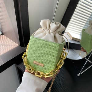 Green bucket bag with vertical pleats and chunky gold chain strap held by a person