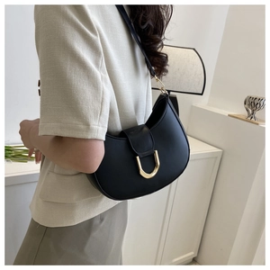 Détail d'un sac à bandoulière demi-lune noir avec boucle dorée en U sur un modèle